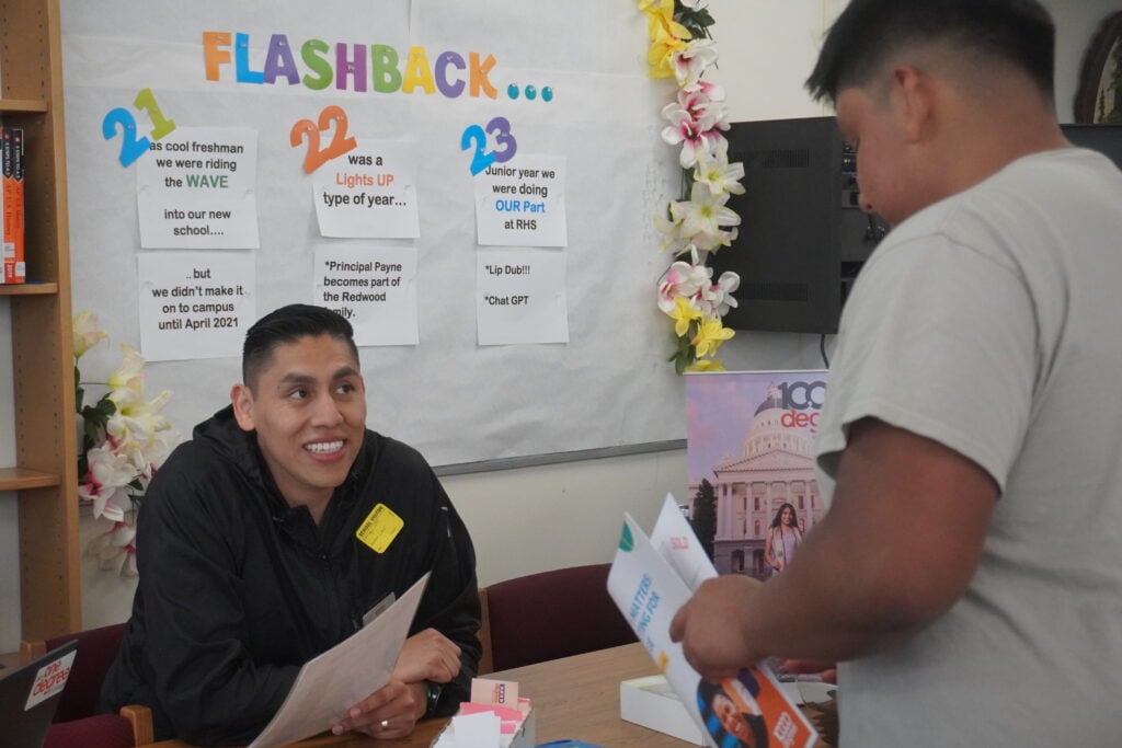 Two men discussing at a school event table.