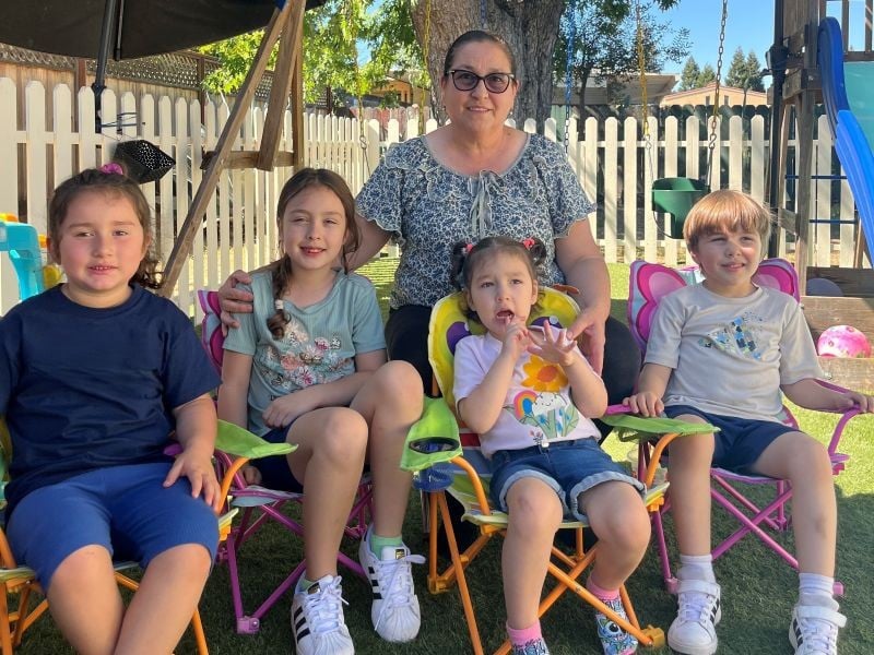 Woman with four kids sitting on chairs outdoors.