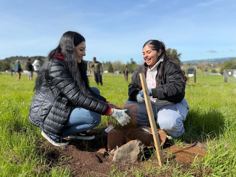 Two women planting a tree in a field.
