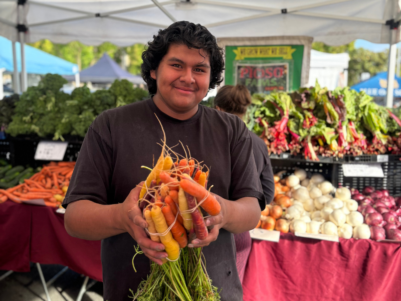 Vendor holding colorful carrots at farmers market.