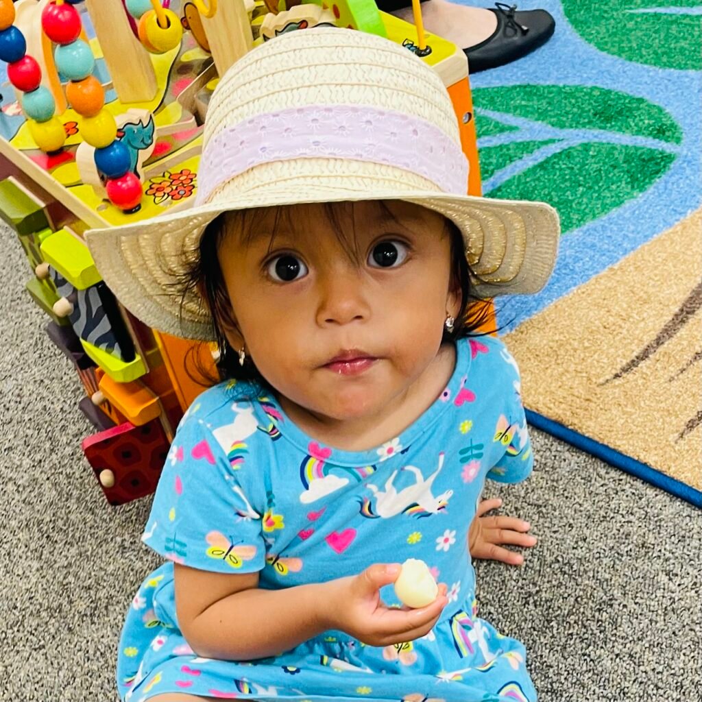 Child wearing hat, playing with toy in playroom.