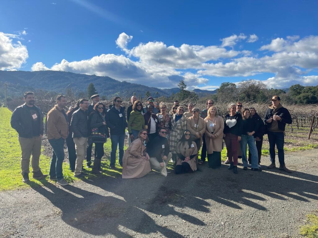 Group of people outdoors at vineyard under blue sky.