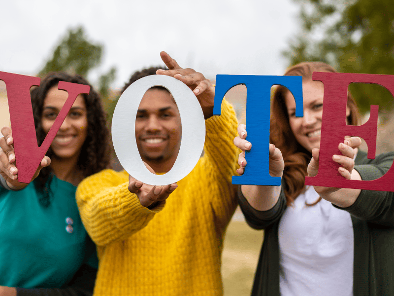 Diverse group holding VOTE sign outdoors.