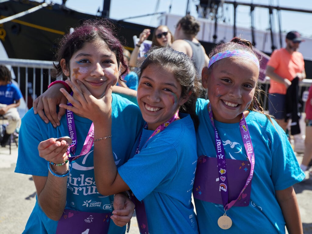 Three girls smiling at outdoor event with medals.