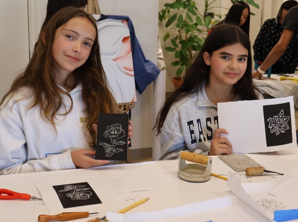 Two girls displaying flower art prints in classroom.