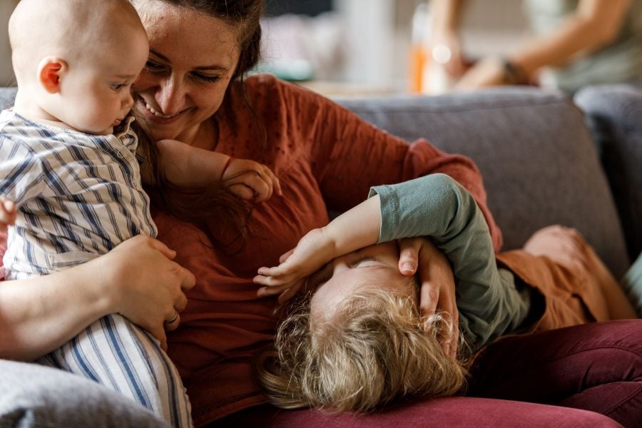 Mother cuddling with two children on couch.