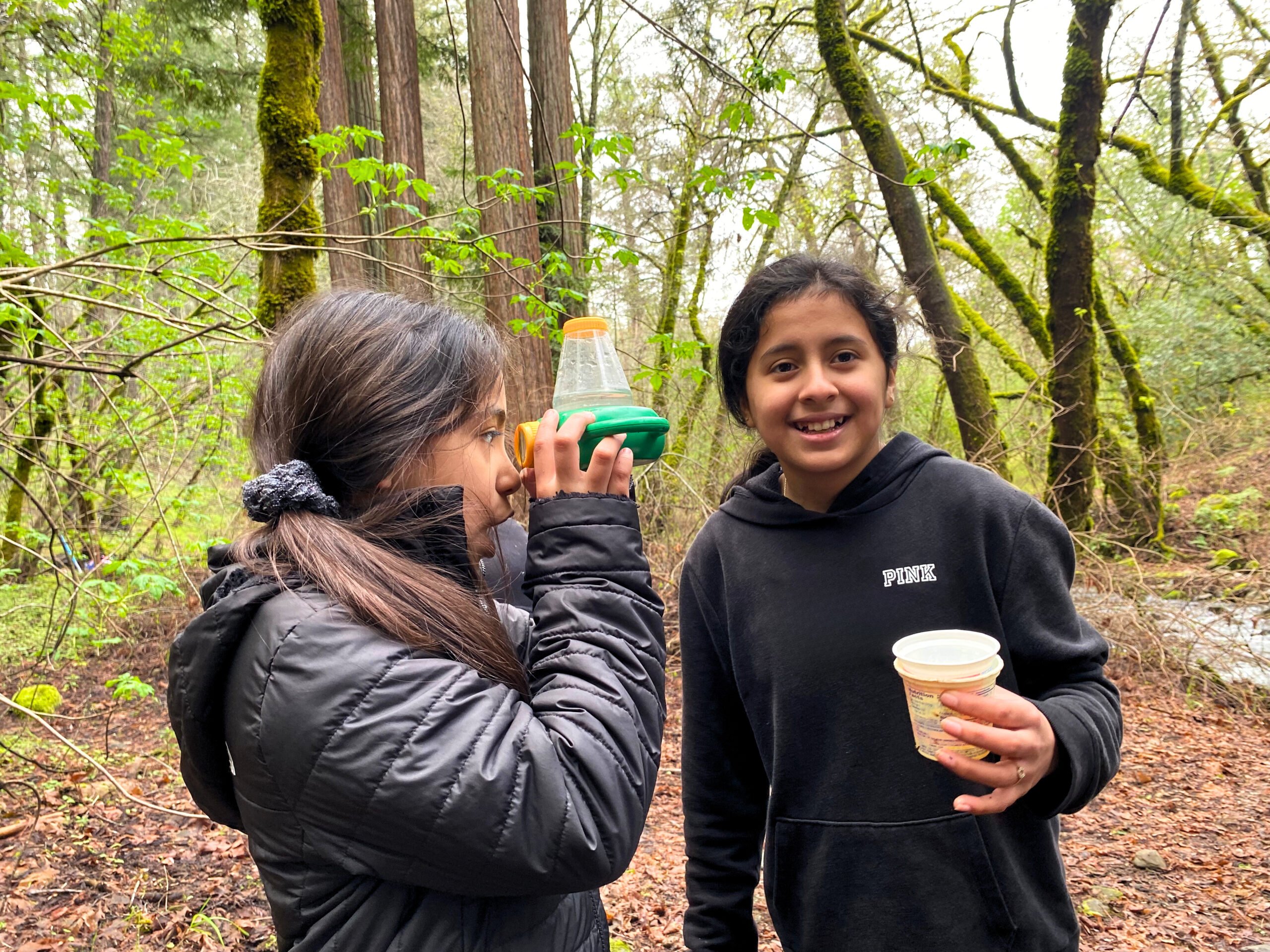 Two girls in forest with nature exploration kits.