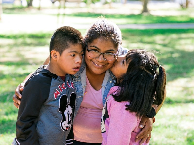 Smiling woman with two affectionate children outdoors.