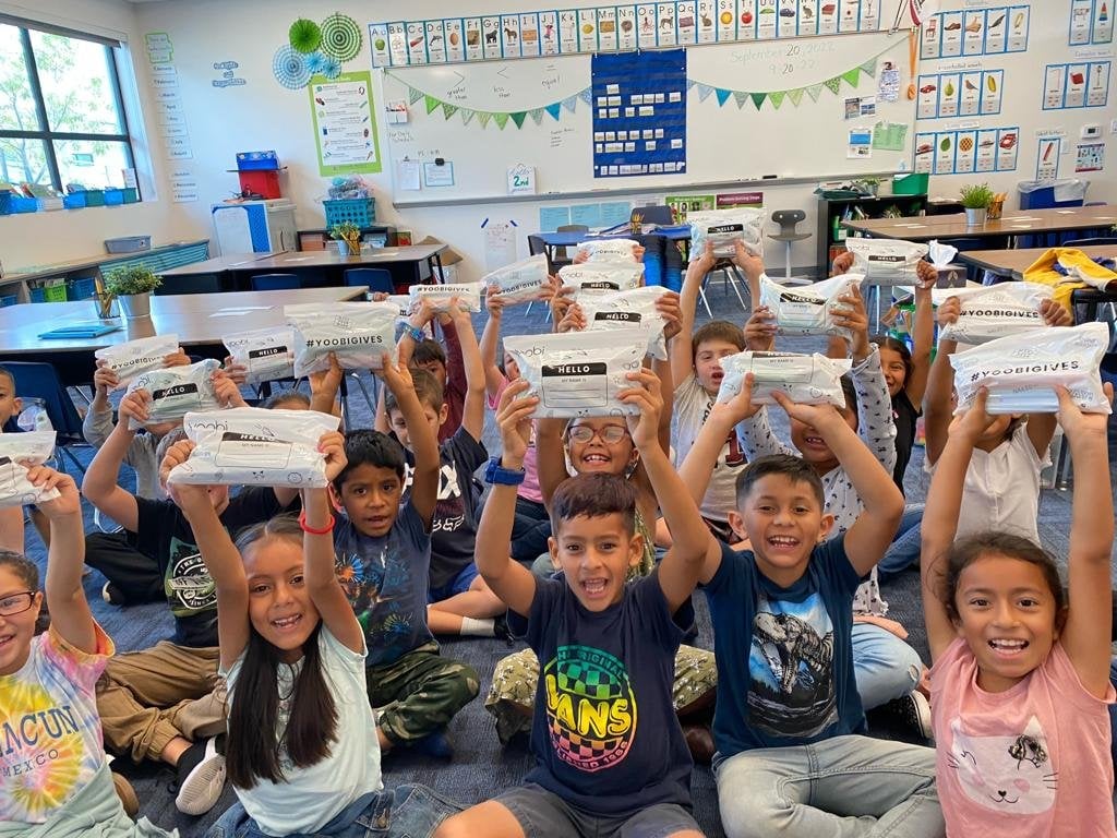 Happy children holding donation bags in classroom.