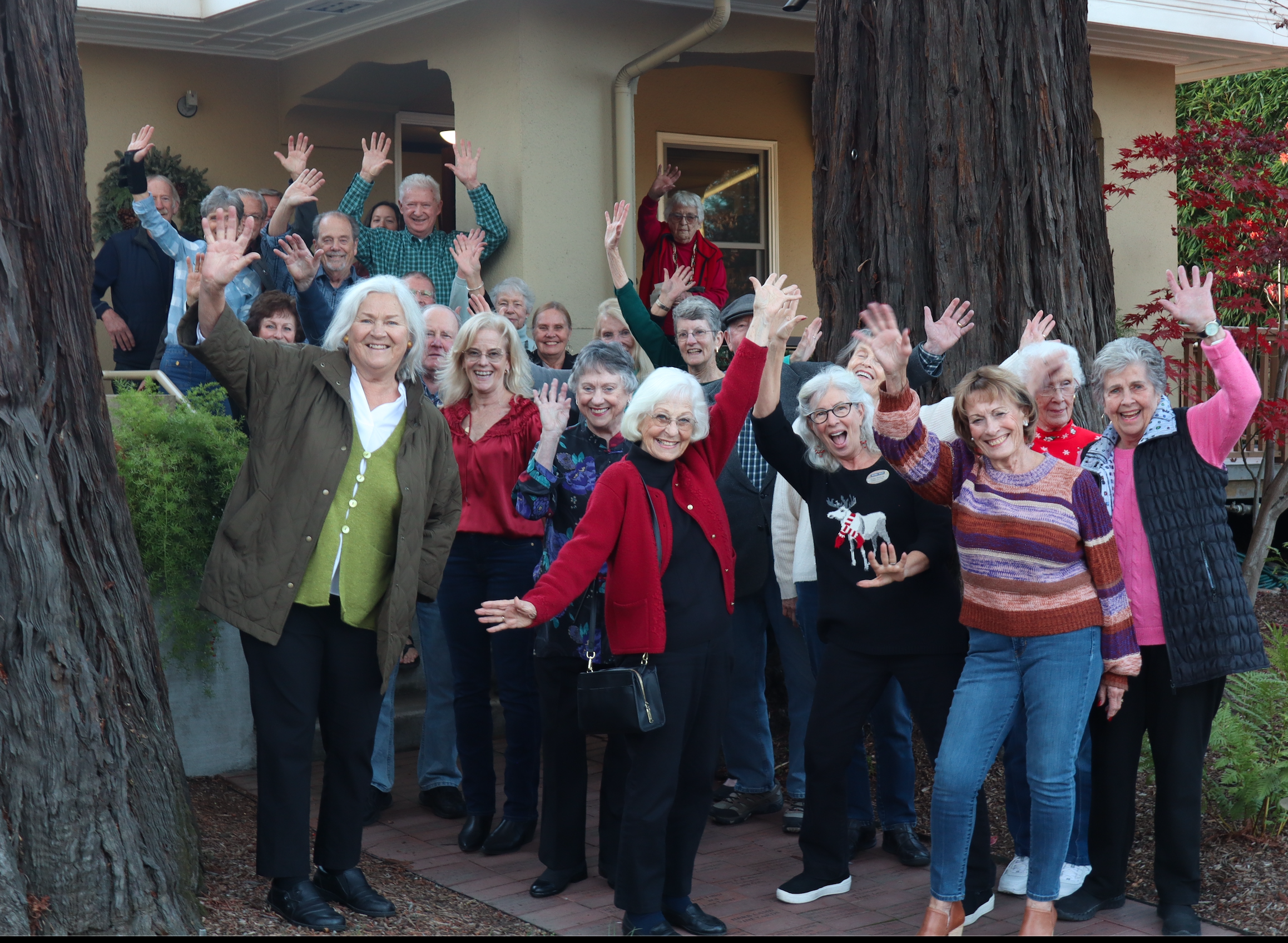 Group of smiling people waving outdoors.