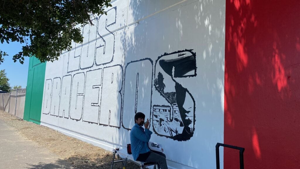 Artist painting Los Braceros mural on wall.