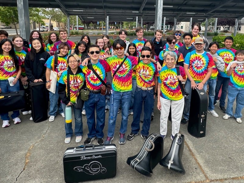 Group in tie-dye shirts with musical instruments.