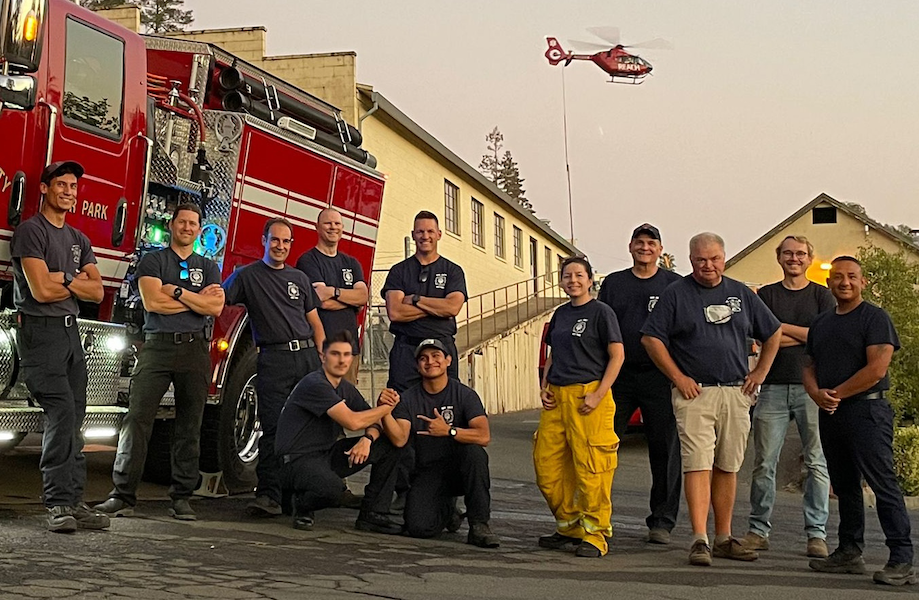 Firefighters pose with fire truck and helicopter.