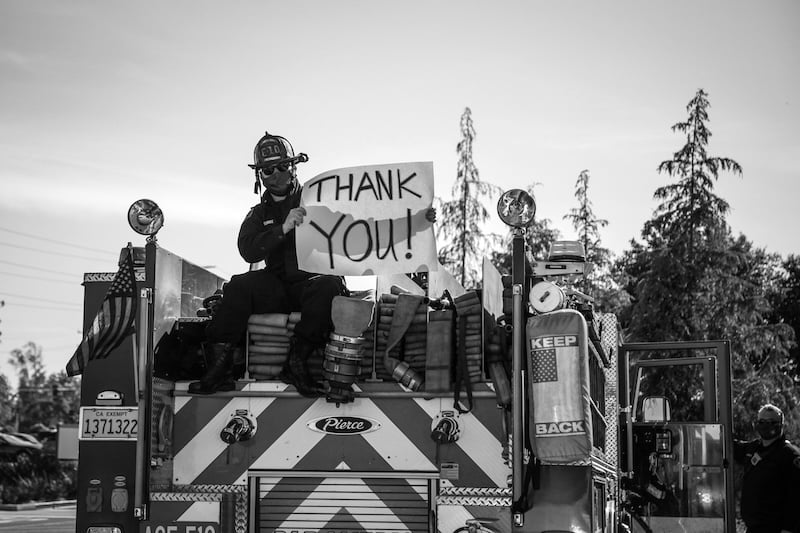 Firefighter holding 'Thank You' sign on fire truck.